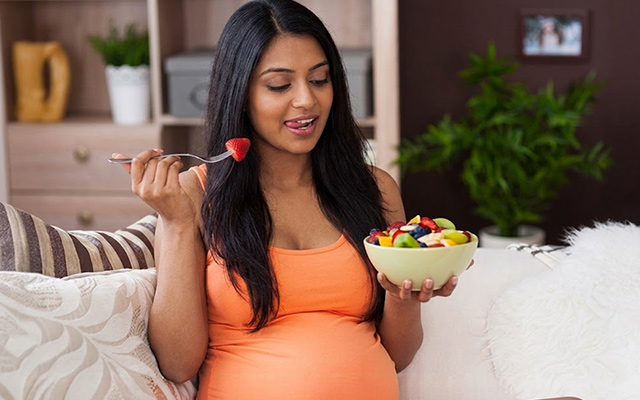 Pregnant woman in a casual setting enjoying a bowl of fresh fruit, promoting healthy eating and nutrient-rich snacks.